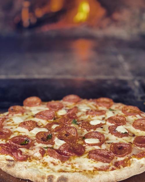 A freshly baked pizza topped with pepperoni and cheese, with a warm, glowing oven in the background.
