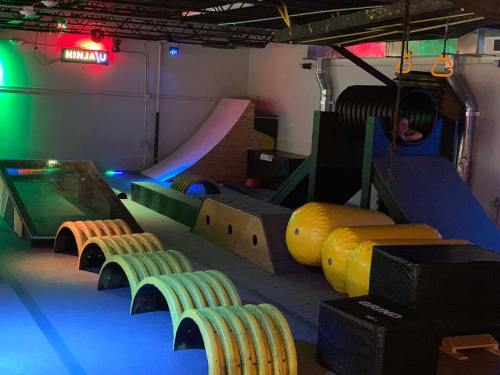 A colorful indoor obstacle course featuring ramps, tunnels, and various climbing structures under vibrant lights.