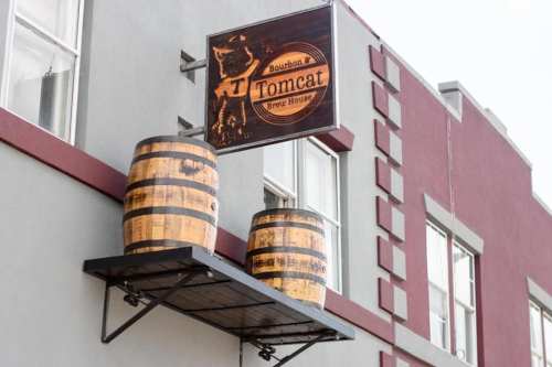 Sign for Tomcat Brew House featuring barrels, mounted on a building with a maroon and gray exterior.