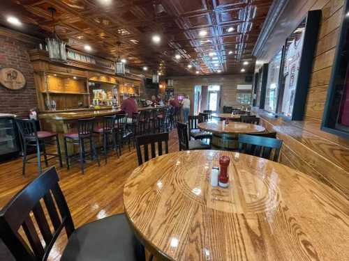 Cozy restaurant interior with wooden tables, a bar, and patrons enjoying their time. Warm lighting and rustic decor.