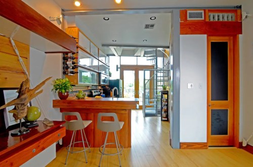 Modern kitchen with wooden accents, bar seating, and a spiral staircase leading to an upper level. Bright and open design.