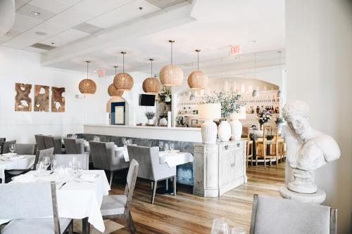A modern restaurant interior featuring wooden floors, elegant tables, and decorative lighting with a bar in the background.