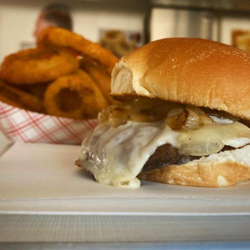 A close-up of a cheeseburger with melted cheese and sautéed onions, alongside a basket of onion rings.