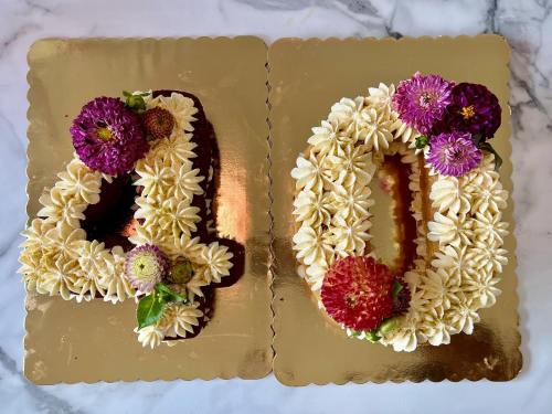 A decorative cake shaped like the numbers 4 and 0, adorned with flowers and cream frosting on a gold background.