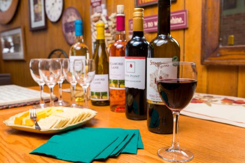 A wooden table set with wine bottles, glasses, cheese, and crackers, creating a cozy tasting atmosphere.