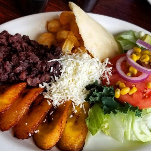 A plate of food featuring black beans, fried plantains, cheese, salad, and an arepa with tomato and corn.