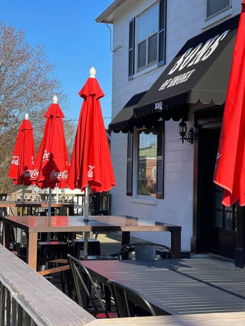 Outdoor dining area with red umbrellas, tables, and a restaurant building in the background.