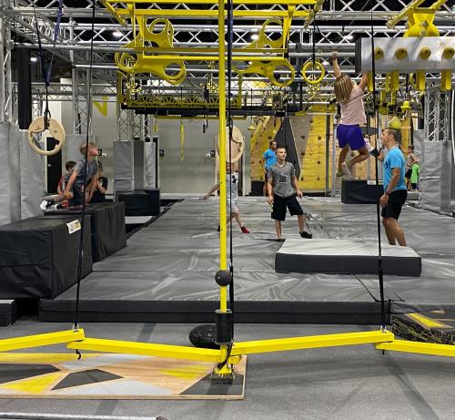 A vibrant indoor obstacle course with kids navigating various challenges and climbing structures.