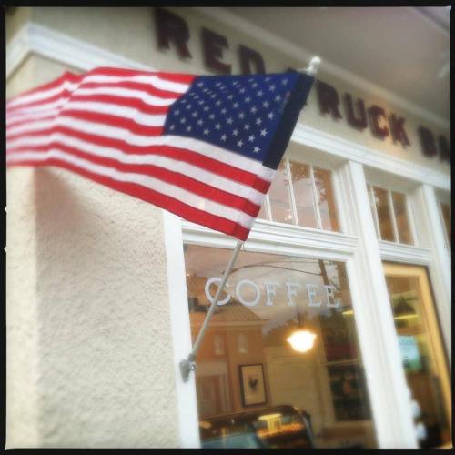 An American flag waves outside a coffee shop with "COFFEE" displayed in the window.