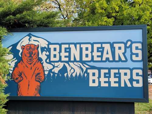 Sign for "Benbear's Beers" featuring a bear illustration and mountain backdrop.