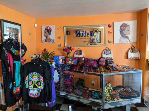 Colorful shop interior featuring traditional Mexican clothing, accessories, and artwork on orange walls.