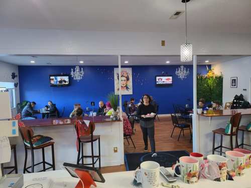 A cozy café interior with blue walls, patrons seated at tables, and a server carrying a tray.