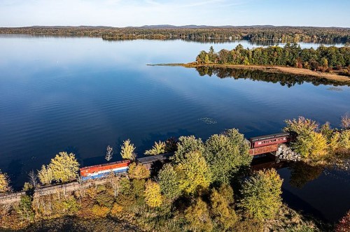 A scenic view of a train along a lakeside, surrounded by colorful autumn foliage and calm waters.