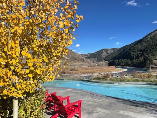 A serene poolside view with red chairs, surrounded by autumn trees and mountains under a clear blue sky.
