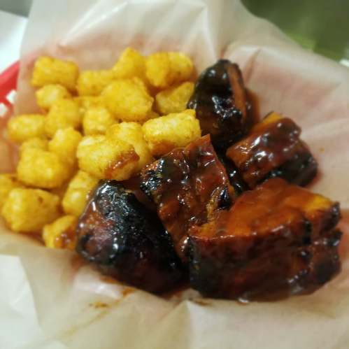 A basket of crispy tater tots alongside glazed barbecue ribs on parchment paper.