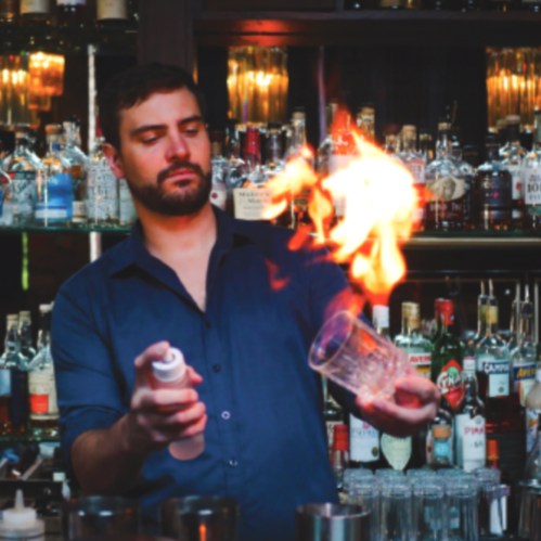 A bartender skillfully ignites a cocktail, surrounded by shelves of various liquor bottles.