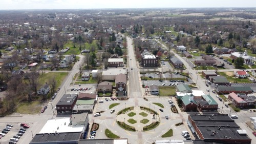Aerial view of a small town featuring a circular intersection, lined with buildings and greenery in the background.