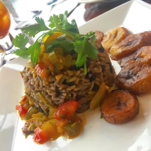 A plate of rice topped with colorful vegetables and cilantro, accompanied by fried plantains.