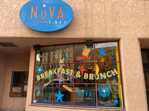 Exterior of Nova Café featuring a bright sign, "OPEN," and colorful decorations promoting breakfast and brunch.