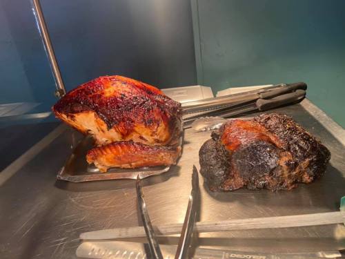 Two large pieces of cooked meat on a metal tray, one with a crispy exterior and the other charred. Tongs are nearby.