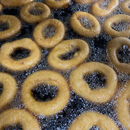 Golden doughnuts frying in bubbling oil, forming perfect circular shapes with holes in the center.