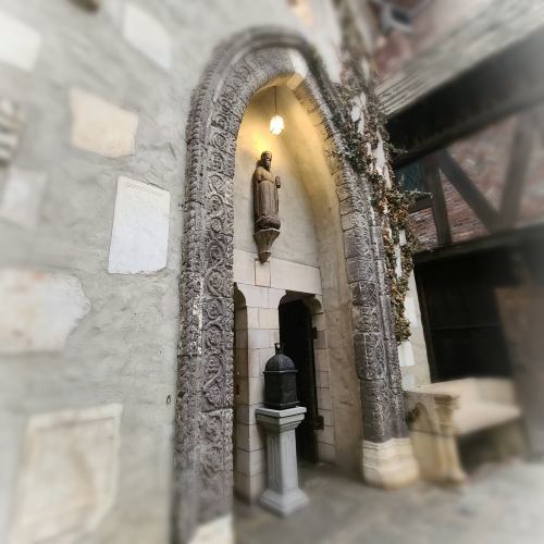 A stone archway with intricate carvings, featuring a statue and a small pedestal, surrounded by ivy.