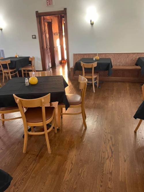 A dining area with wooden floors, black tablecloths on tables, and a door leading to another room.