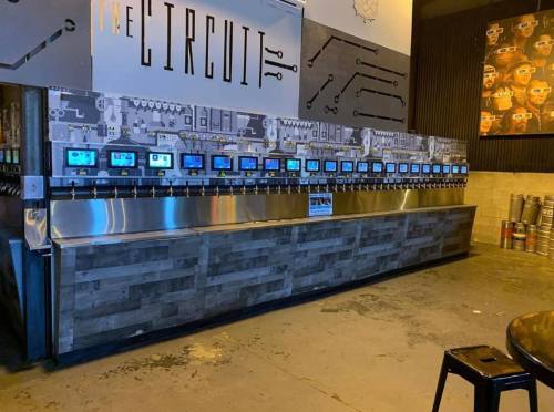 A modern self-serve beverage station with multiple taps and screens, set in a stylish bar environment.