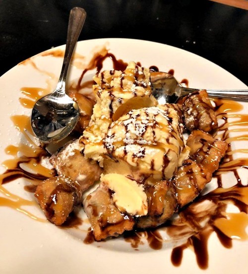 A dessert plate featuring fried dough, ice cream, and drizzles of chocolate and caramel sauce. Two spoons are beside it.