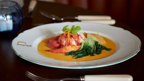 A gourmet dish featuring lobster on a bed of greens, served in a vibrant orange sauce on an elegant plate.
