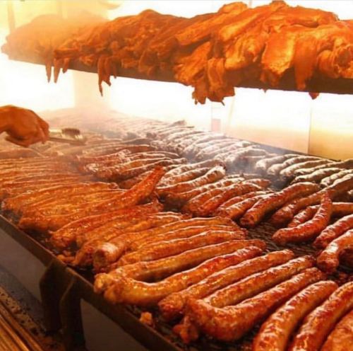 A grill filled with various types of sausages and meats, with smoke rising in a vibrant cooking environment.