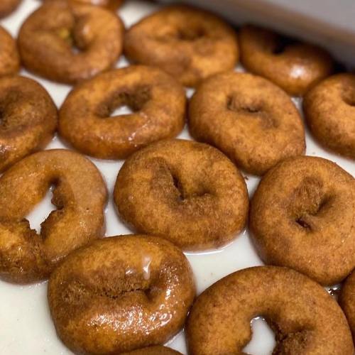 A close-up of freshly made donuts arranged in a tray, coated with a light glaze.