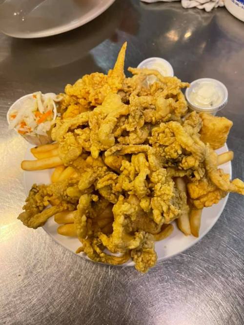 A plate piled high with crispy fried seafood, golden fries, and two cups of dipping sauces.