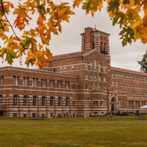 Historic brick building with a tower, surrounded by green grass and autumn leaves.