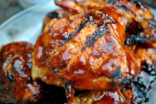 Grilled chicken pieces glazed with a shiny barbecue sauce, showcasing a smoky, charred texture.
