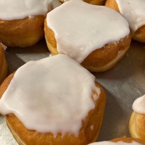 Close-up of glazed donuts with a shiny white icing on a metal tray.