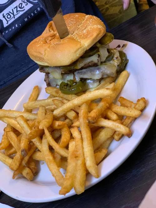 A stacked burger with cheese and jalapeños, served with a side of golden French fries on a white plate.