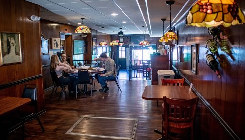 A cozy restaurant interior with wooden walls, stained glass lamps, and diners at a table in the background.