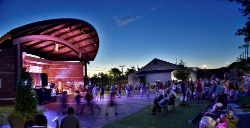A lively outdoor concert at dusk, with a crowd dancing in front of a stage under a colorful sky.