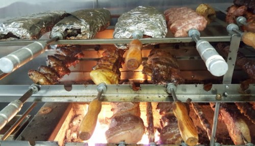 A grill with various meats on skewers, including foil-wrapped items, cooking over an open flame.
