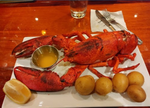 A plate with a whole lobster, melted butter, lemon wedge, and boiled potatoes on a wooden table.