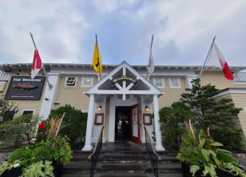 Exterior of a restaurant with flags, a sign reading "The Mooring," and lush greenery in front.