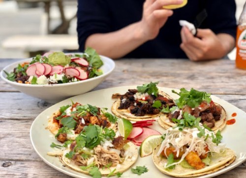 A plate of tacos topped with cilantro and lime, alongside a fresh salad and a bottle of soda.