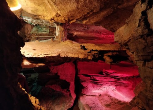 Colorful rock formations illuminated by lights in a cave, showcasing layers of stone and unique textures.