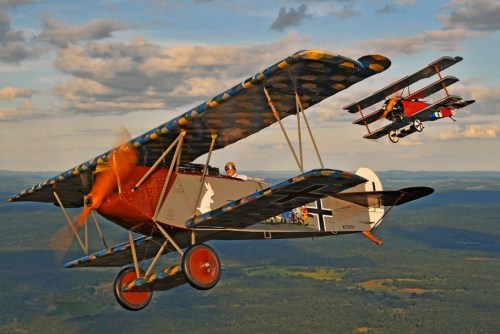 Two vintage biplanes flying in formation against a scenic sky, showcasing colorful patterns and historical designs.
