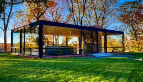 A modern glass house surrounded by trees and colorful autumn foliage, set on a green lawn.