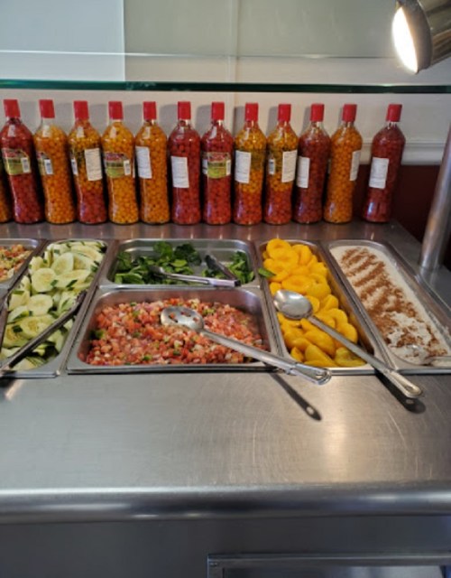 A buffet table with various salads, fruits, and colorful bottles of condiments in the background.