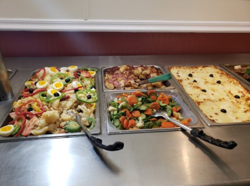 A buffet display featuring colorful salads, roasted vegetables, and a cheesy pasta dish.