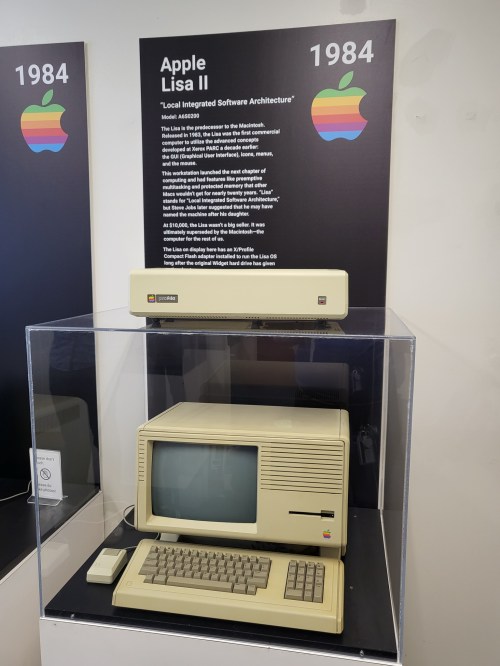 An Apple Lisa II computer from 1984 displayed in a glass case with an informational sign.