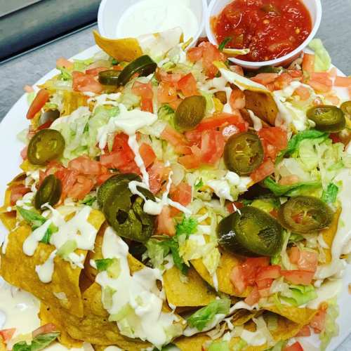 A plate of nachos topped with lettuce, tomatoes, jalapeños, and drizzled with sauce, served with salsa and sour cream.
